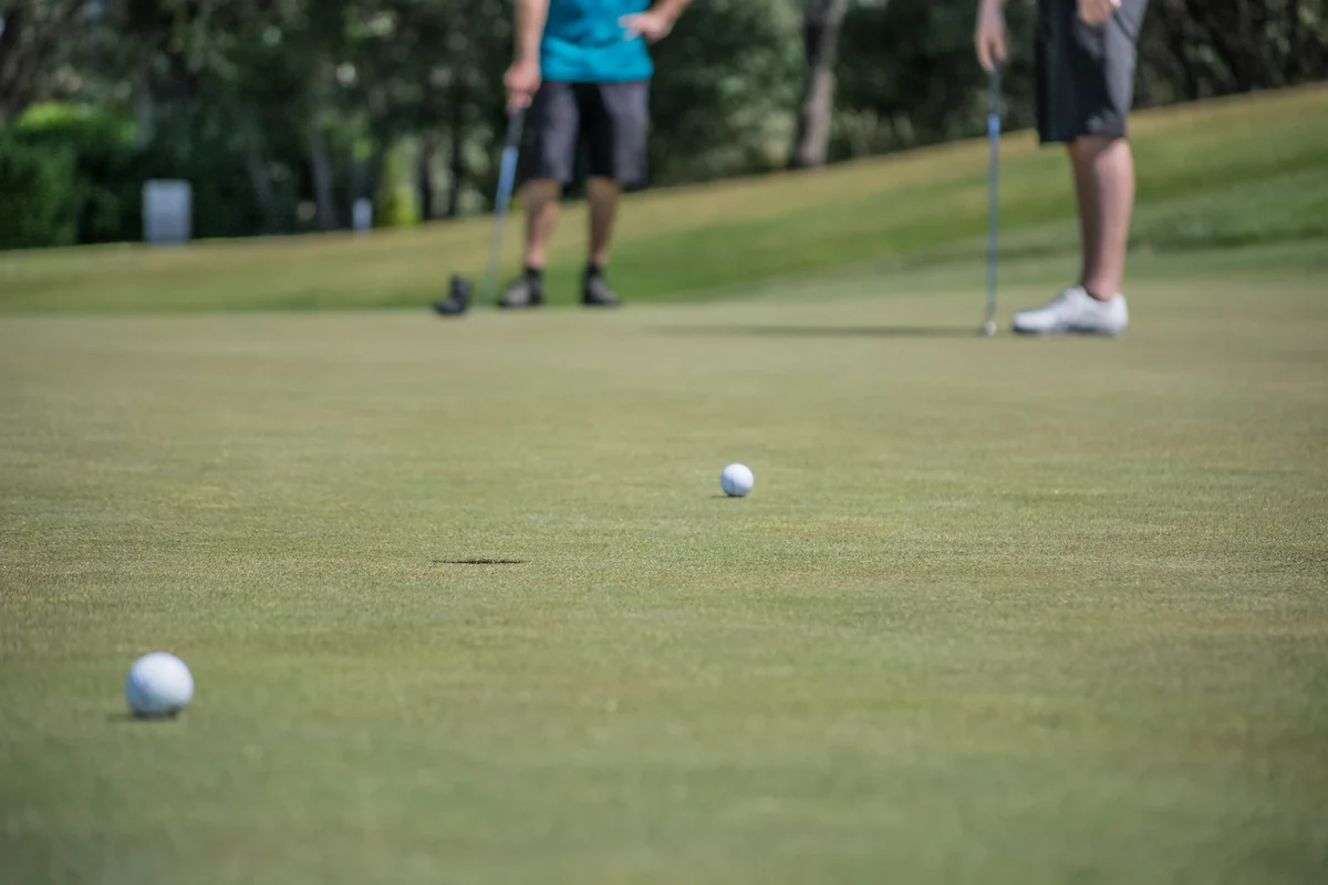 Golfers putting on a green with golf balls and clubs in view; illustrative golf photograph, not Raven Golf Club.