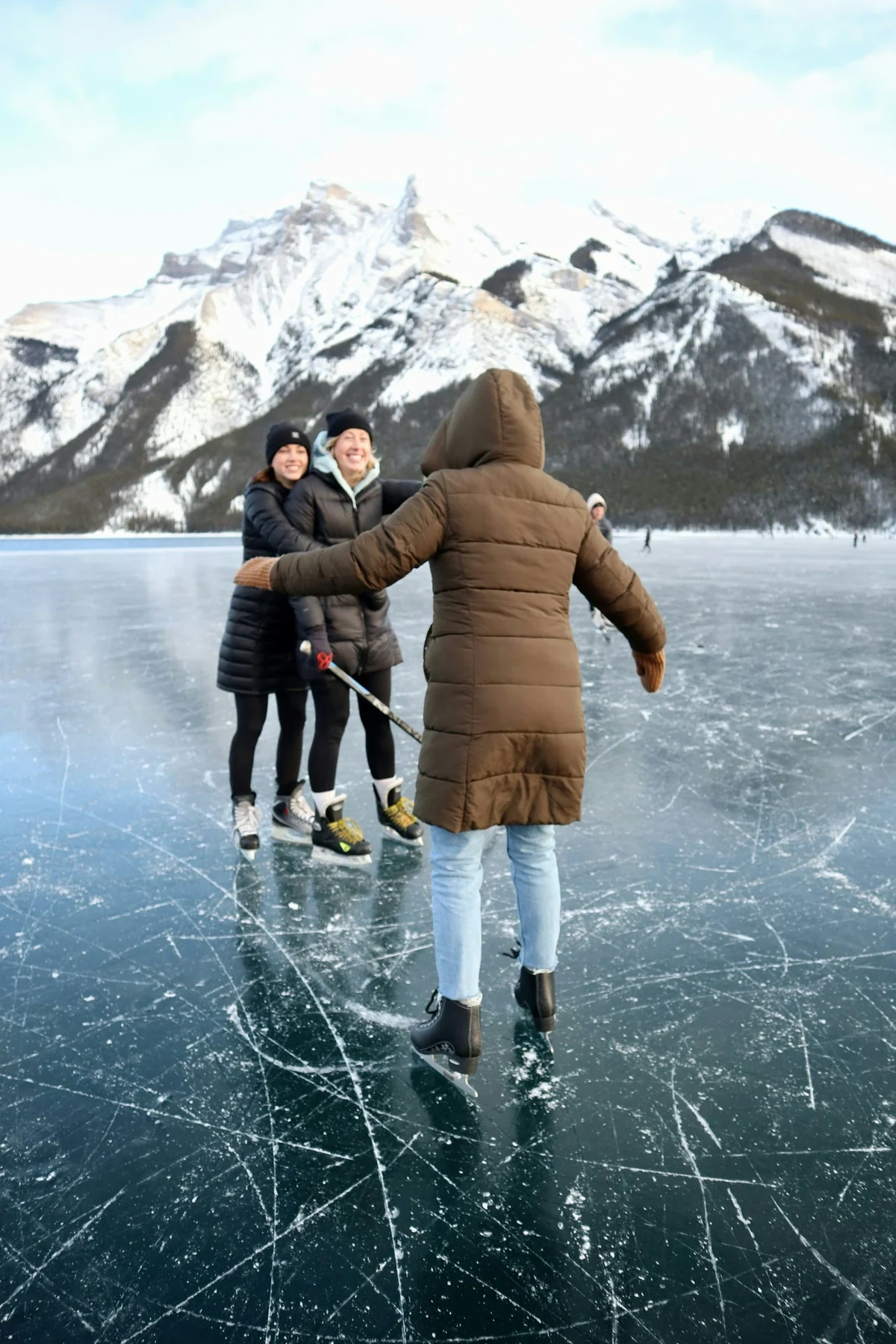 Friends ice skating on a frozen lake beneath snowy mountains; illustrative activity photograph.
