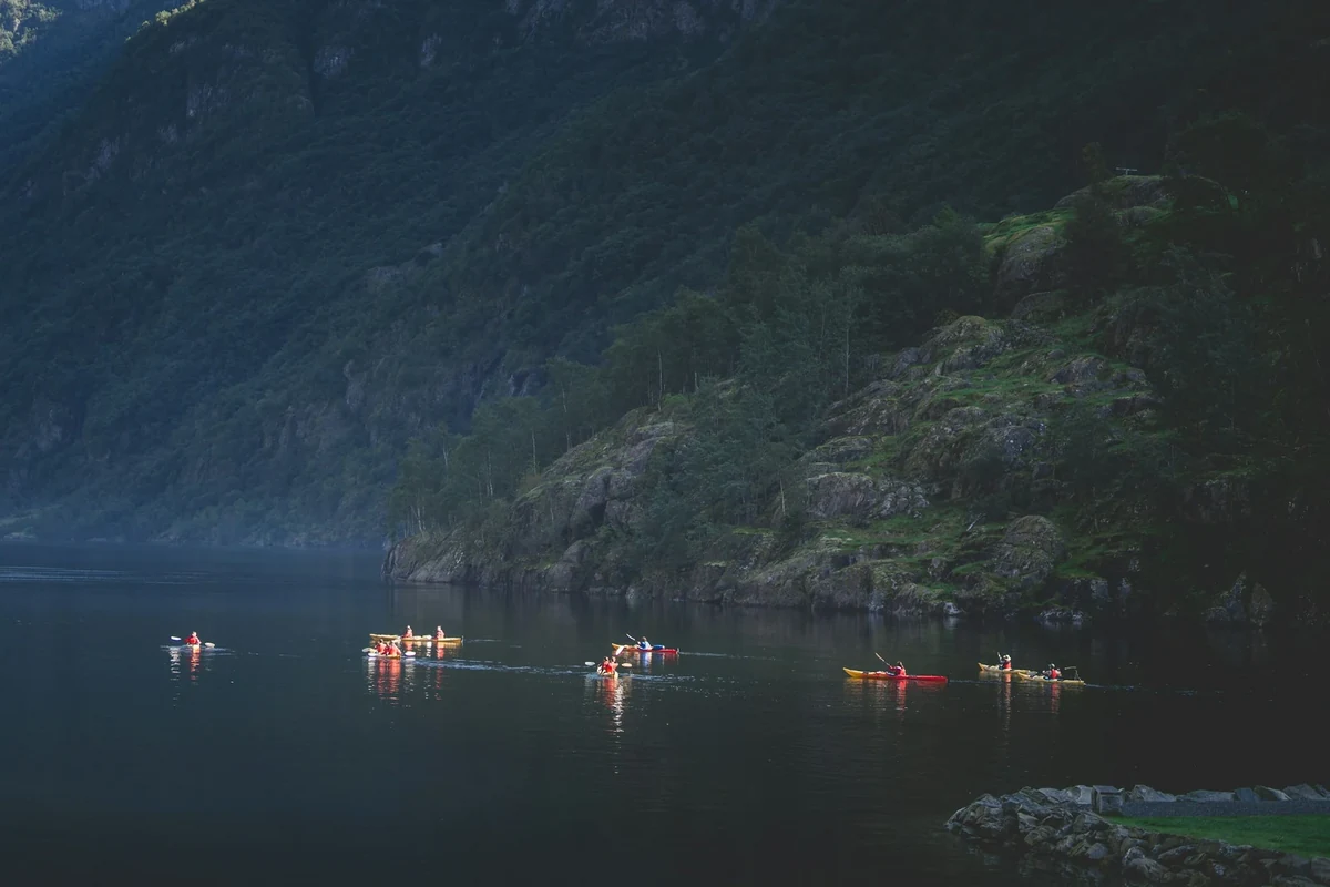 Kayakers on calm water below forested cliffs in Norway. This photograph illustrates paddling, not Dillon Reservoir.