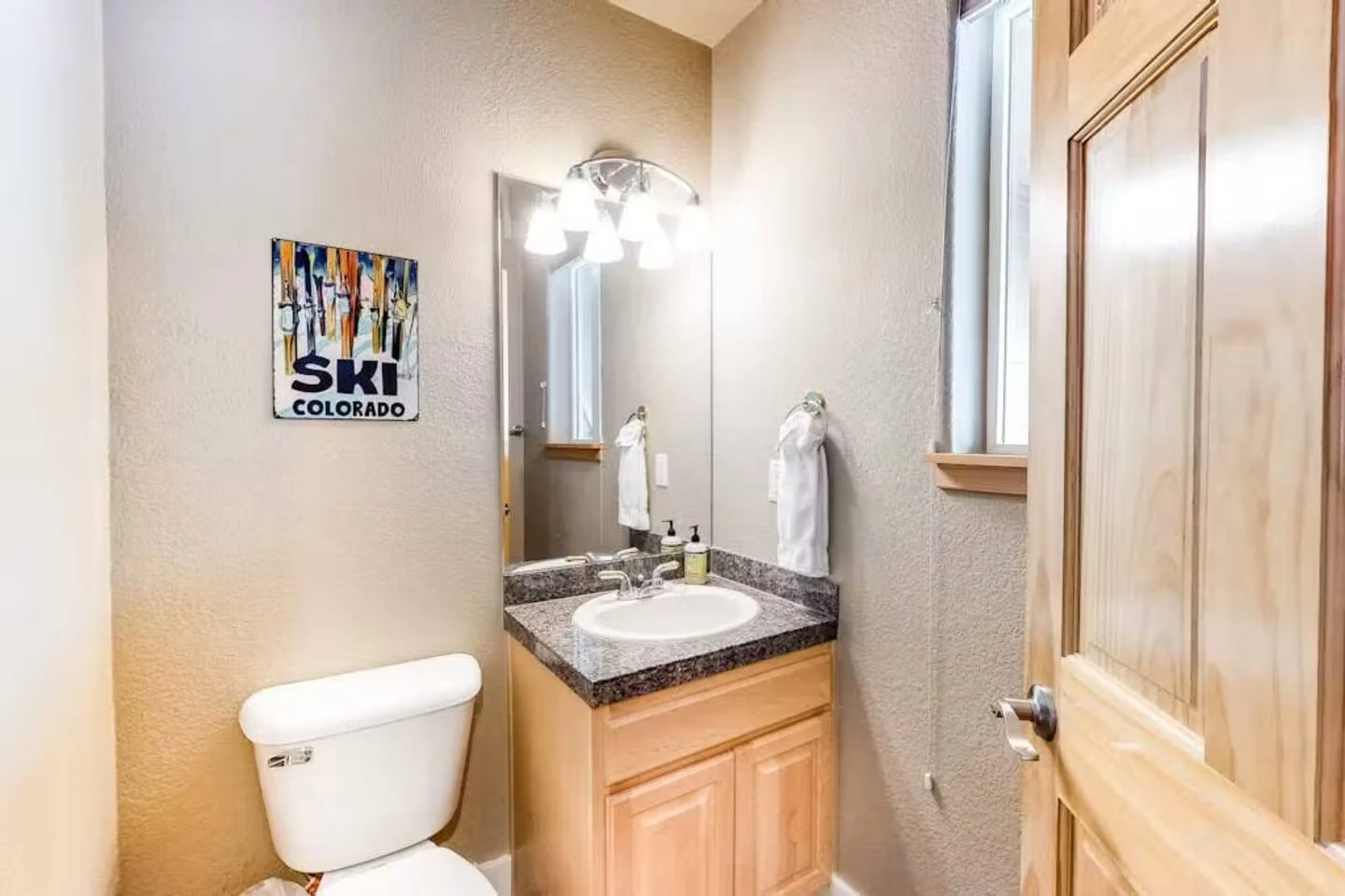 North Pond Retreat, Compact powder room with a toilet, wood vanity, and wall art with a ski theme, waterfront vacation rental in Silverthorne, Colorado