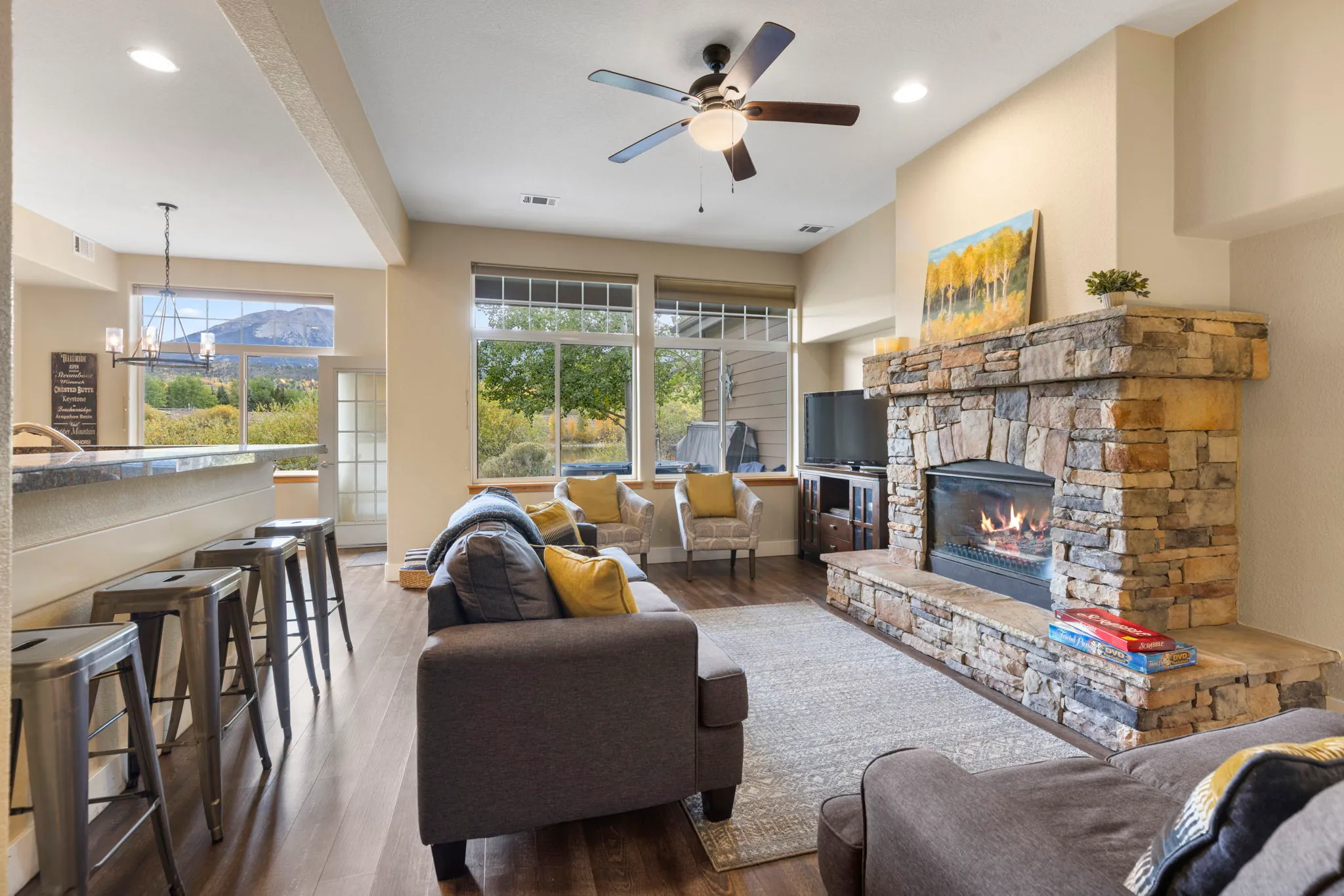North Pond Retreat, Living room with a stone fireplace, gray sofas, large windows, and an open kitchen, waterfront vacation rental in Silverthorne, Colorado