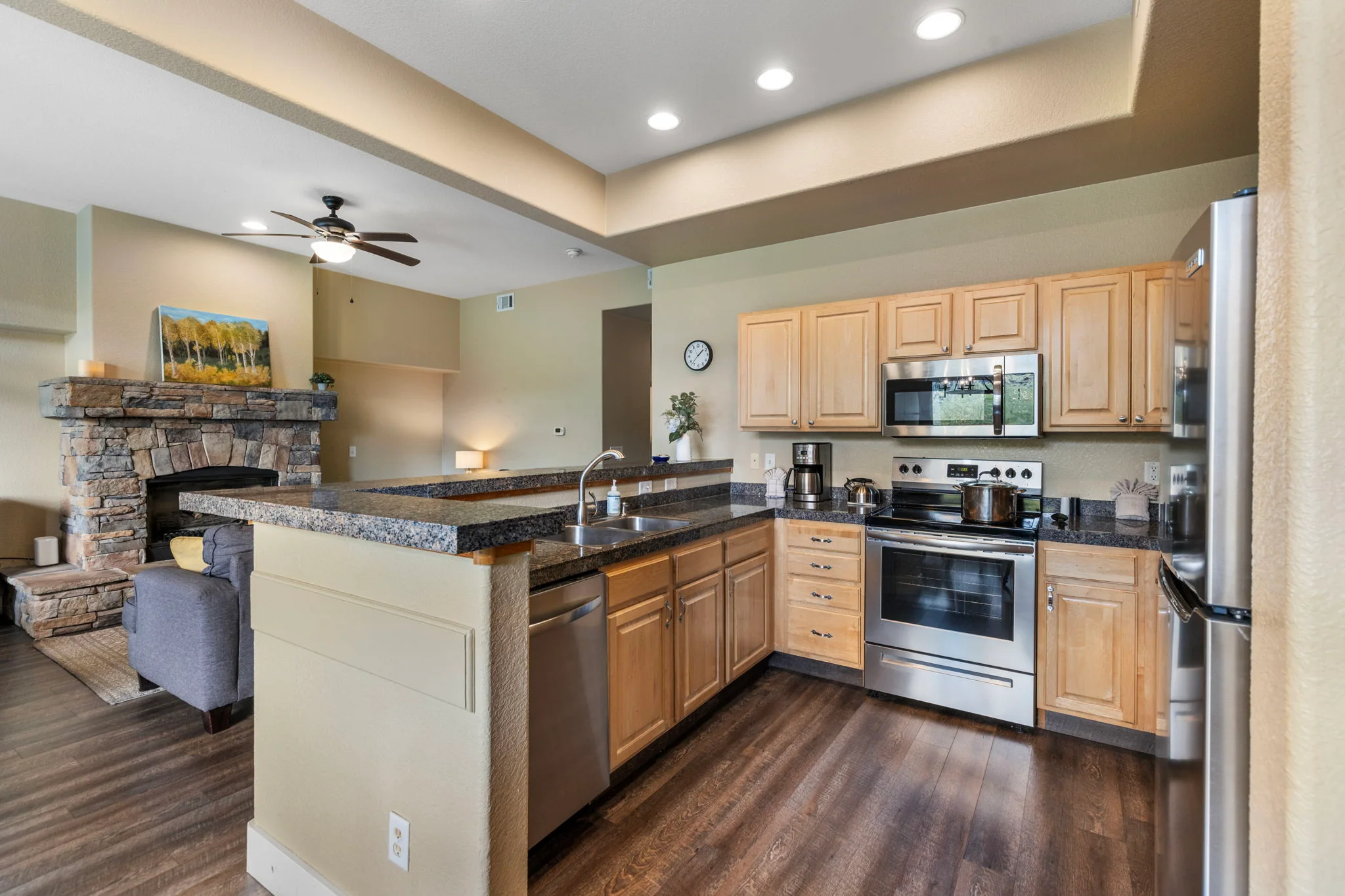 North Pond Retreat, Open kitchen with a stainless stove, wood cabinets, dark countertops, and living room beyond, waterfront vacation rental in Silverthorne, Colorado