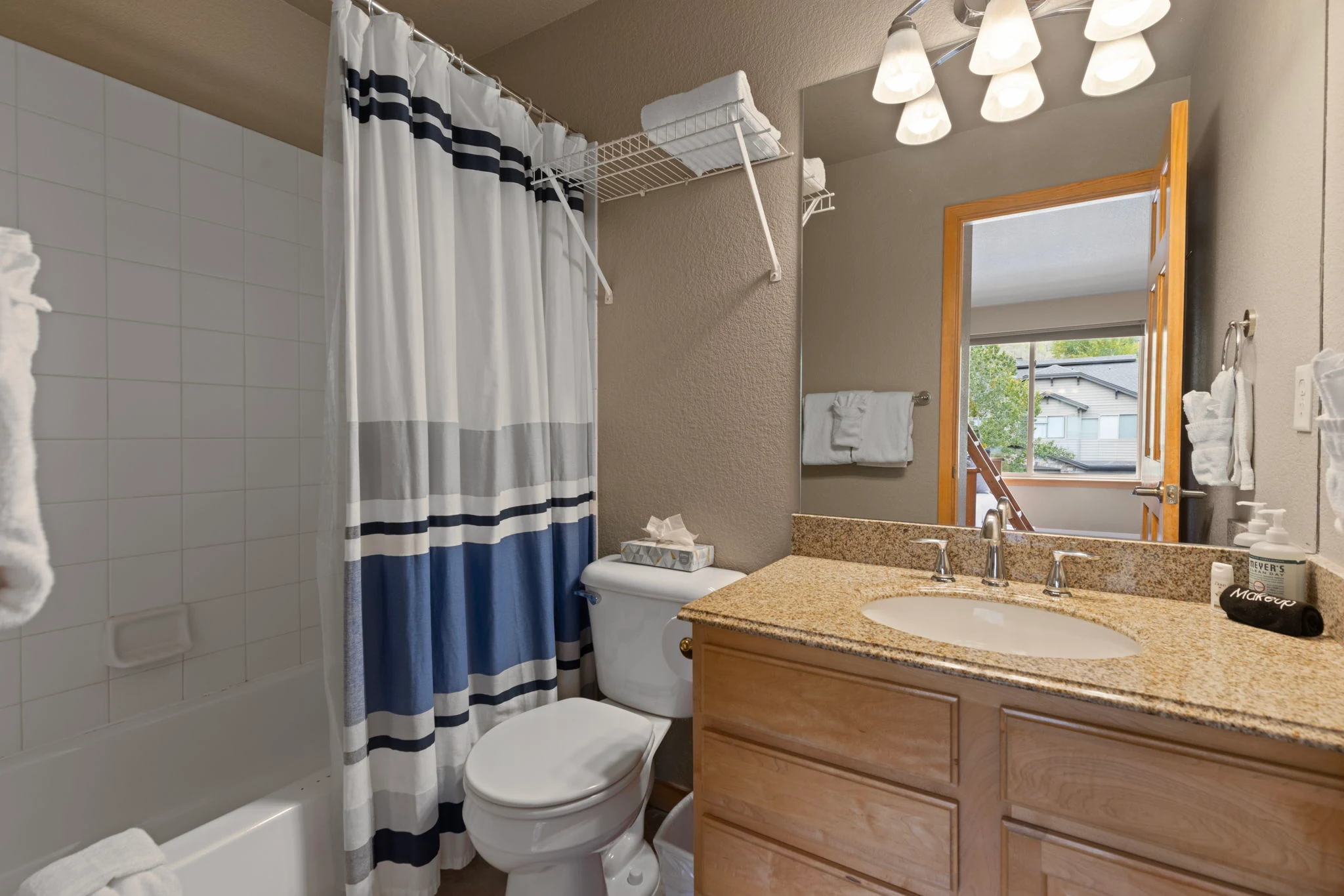 North Pond Retreat, Bathroom with a striped shower curtain, wood vanity, toilet, mirror, and window, waterfront vacation rental in Silverthorne, Colorado