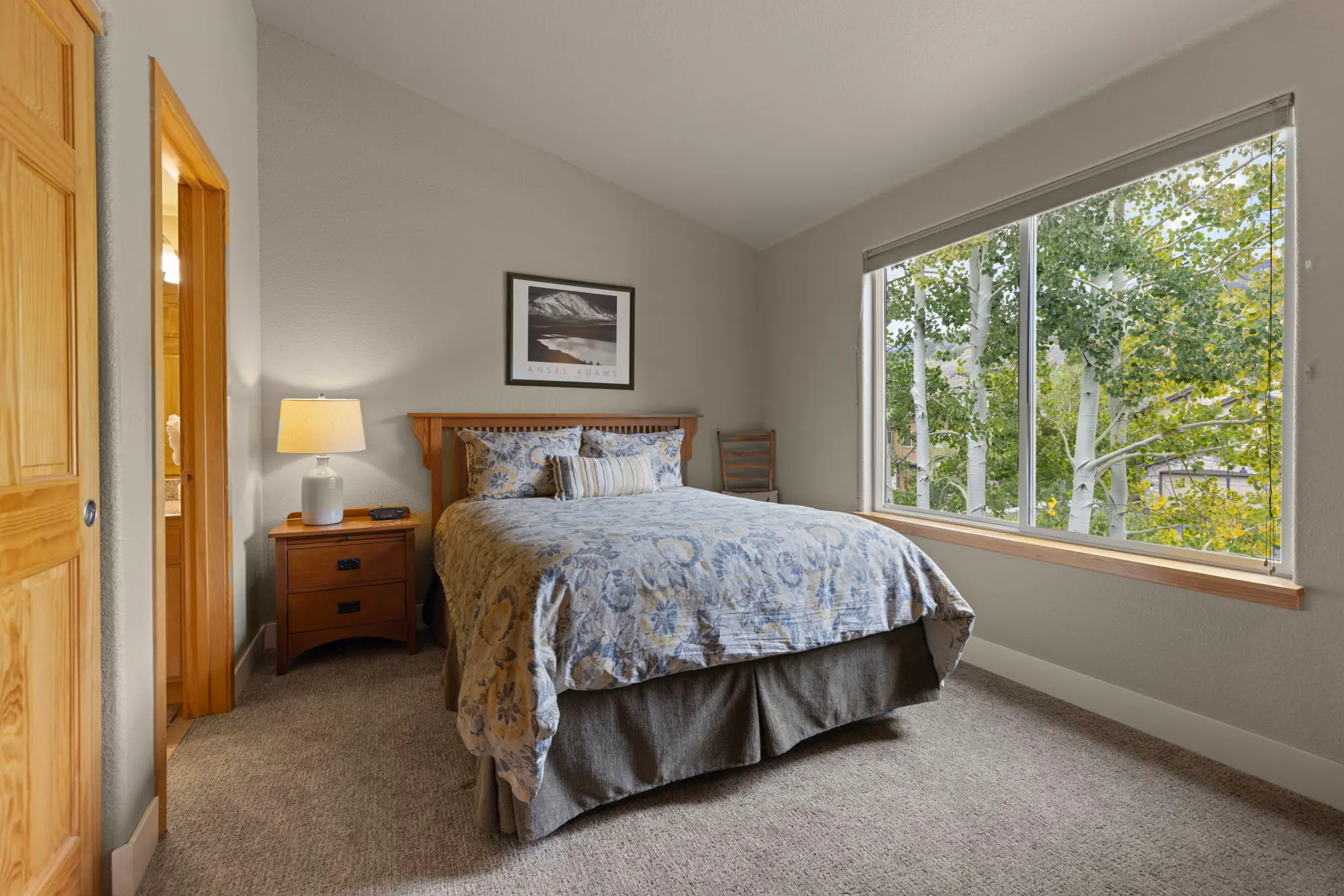 North Pond Retreat, Queen bed with patterned bedding and wood nightstands beside a wide window overlooking trees, waterfront vacation rental in Silverthorne, Colorado