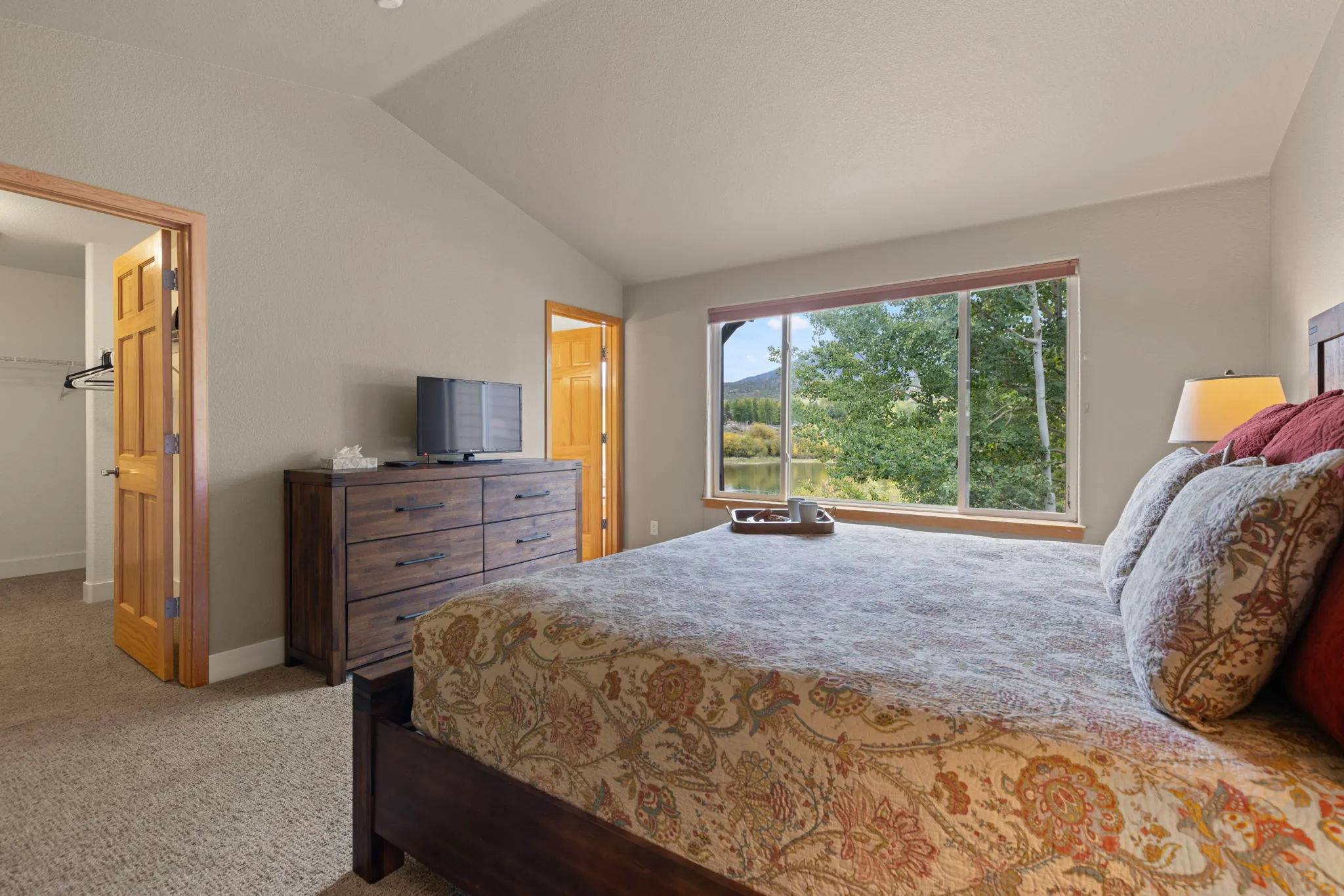 North Pond Retreat, King bed with patterned bedding, pillows, bedside lighting, and windows overlooking trees, waterfront vacation rental in Silverthorne, Colorado
