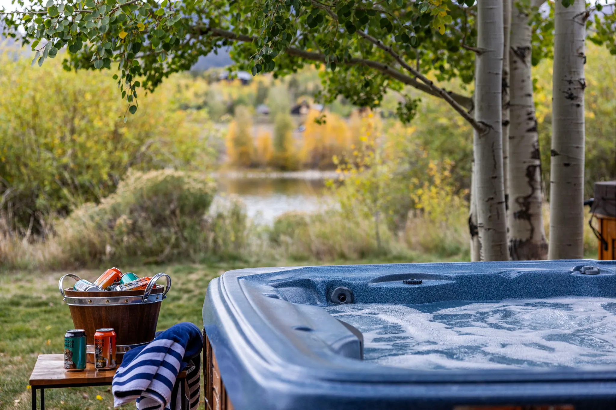 North Pond Retreat, Bubbling hot tub beside a towel and refreshment basket, with trees and the pond beyond, waterfront vacation rental in Silverthorne, Colorado