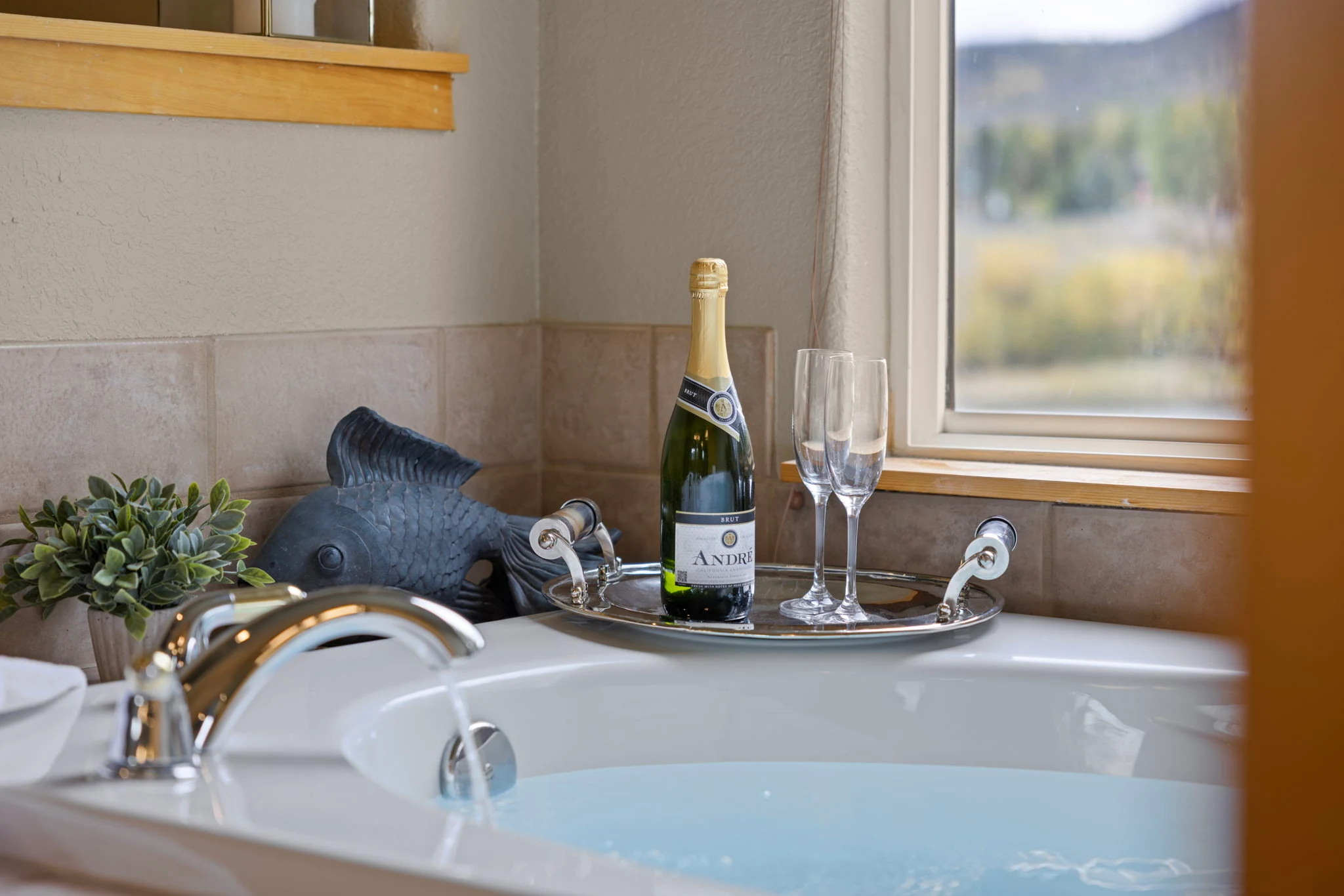 North Pond Retreat, Bathtub with a chrome faucet, towels, flowers, a bottle, and glasses on a tray beside the window, waterfront vacation rental in Silverthorne, Colorado